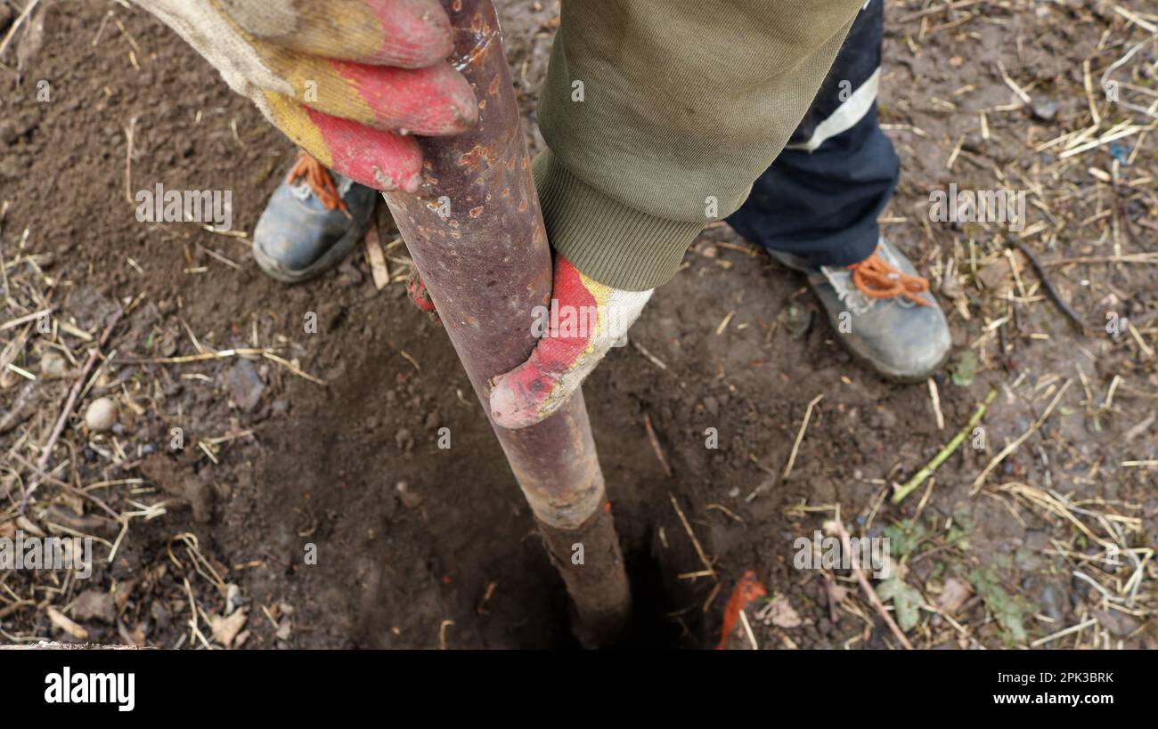a worker pulls an iron rounded rusty pole out of an earthen pit, heavy