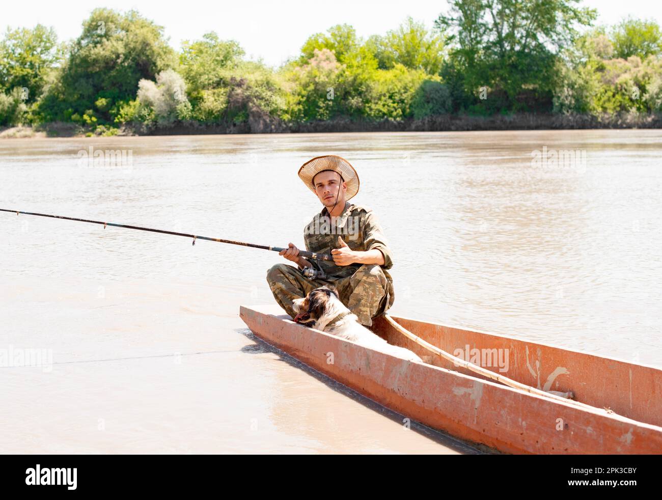 Pensive fisherman in camo outfit carrying fishing pole, while going fishing  with dog in summer day Stock Photo - Alamy