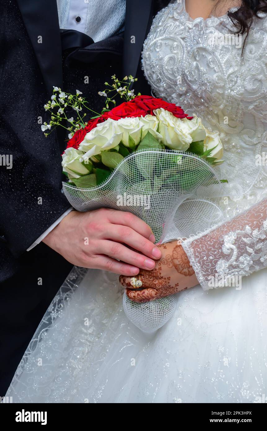 An Arab bride and groom holding a bouquet of flowers with henna tattoos on the bride's hand Stock Photo