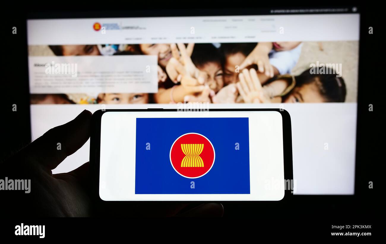 Person holding smartphone with logo of Association of Southeast Asian Nations (ASEAN) on screen in front of website. Focus on phone display. Stock Photo