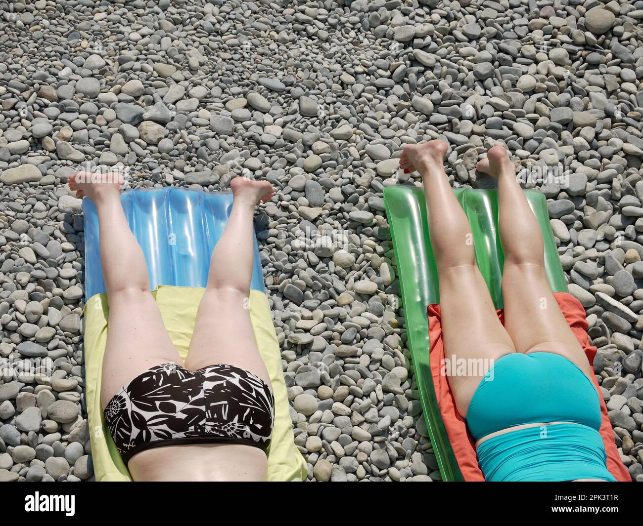 two women sunbathe on colorful inflatable mattresses Stock Photo