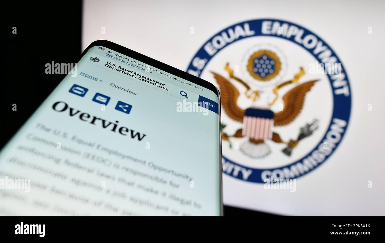 Mobile phone with website of Equal Employment Opportunity Commission (EEOC) on screen in front of logo. Focus on top-left of phone display. Stock Photo