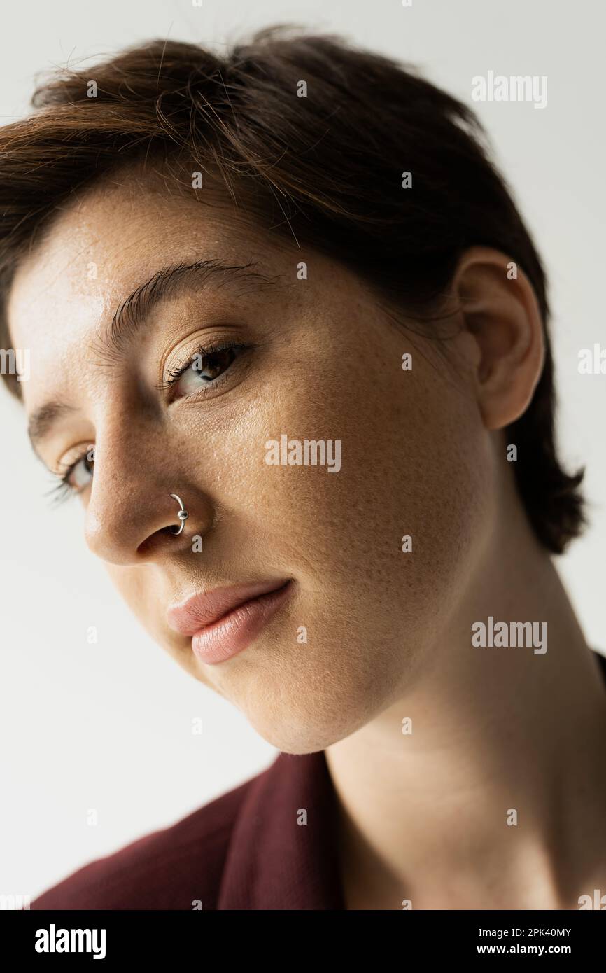 close up portrait of young freckled woman with nose piercing looking at camera isolated on grey,stock image Stock Photo