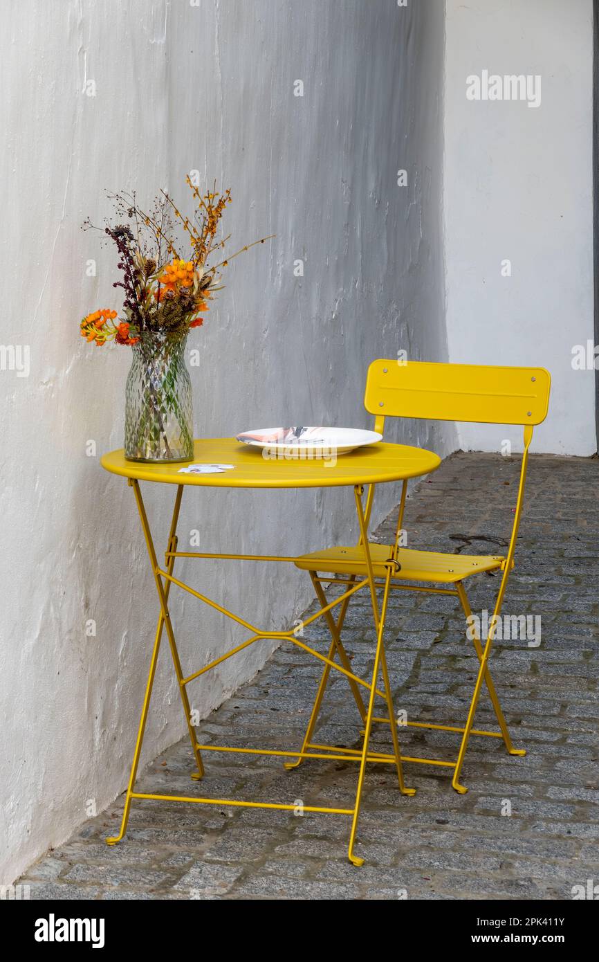 Typical yellow iron table and chair on which there is a plate and a vase with flowers. Stock Photo