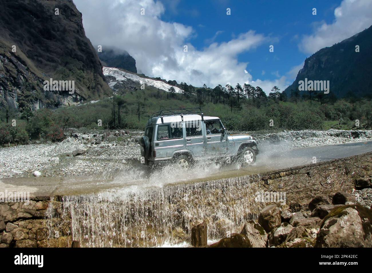 Tourist car crossing fountain at Yumthang Valley or Sikkim Valley of Flowers sanctuary, Himalayan mountains, North Sikkim, India. Shingba Rhododendron Stock Photo