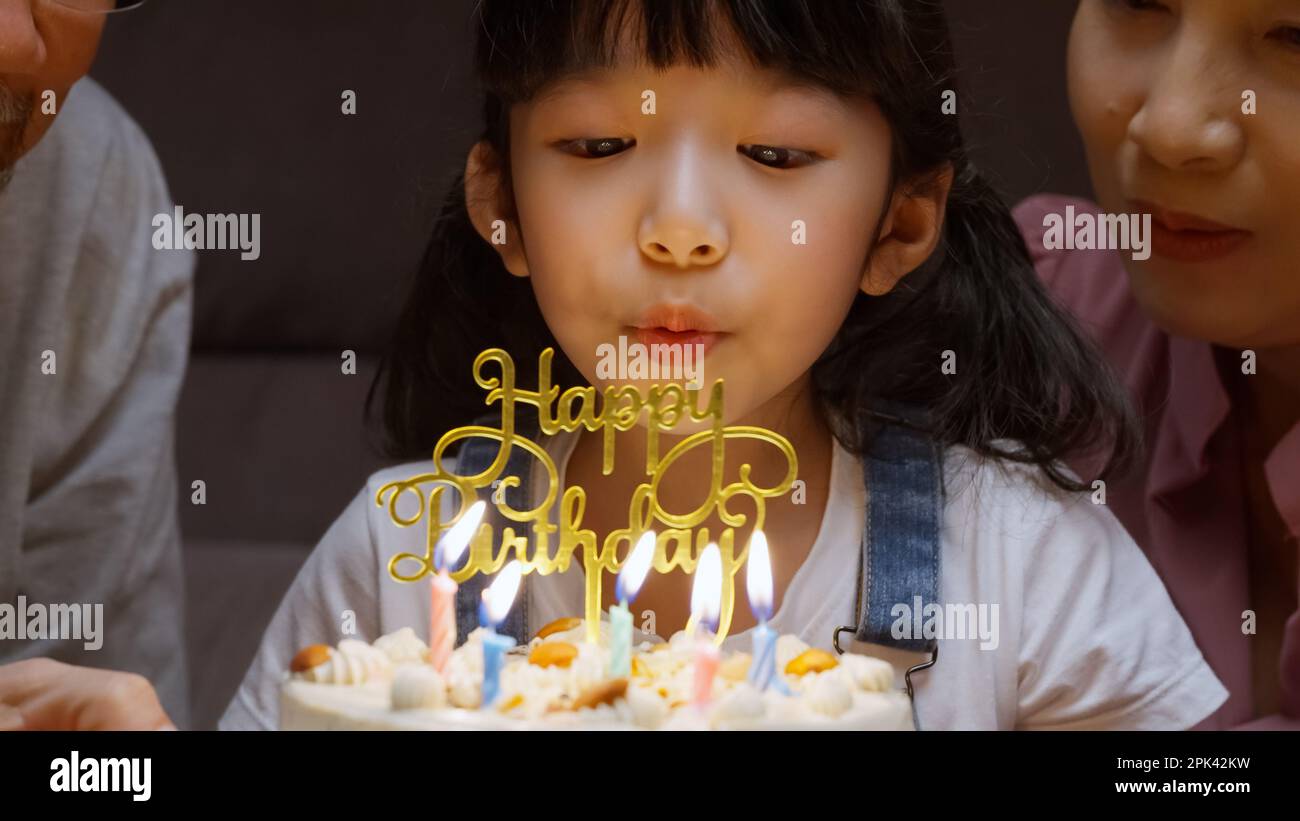 Happy girl surrounded by family making wish and blowing out candles on