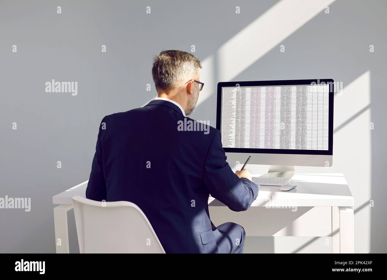 Businessman or accountant at workplace compares data on electronic spreadsheet on computer. Stock Photo