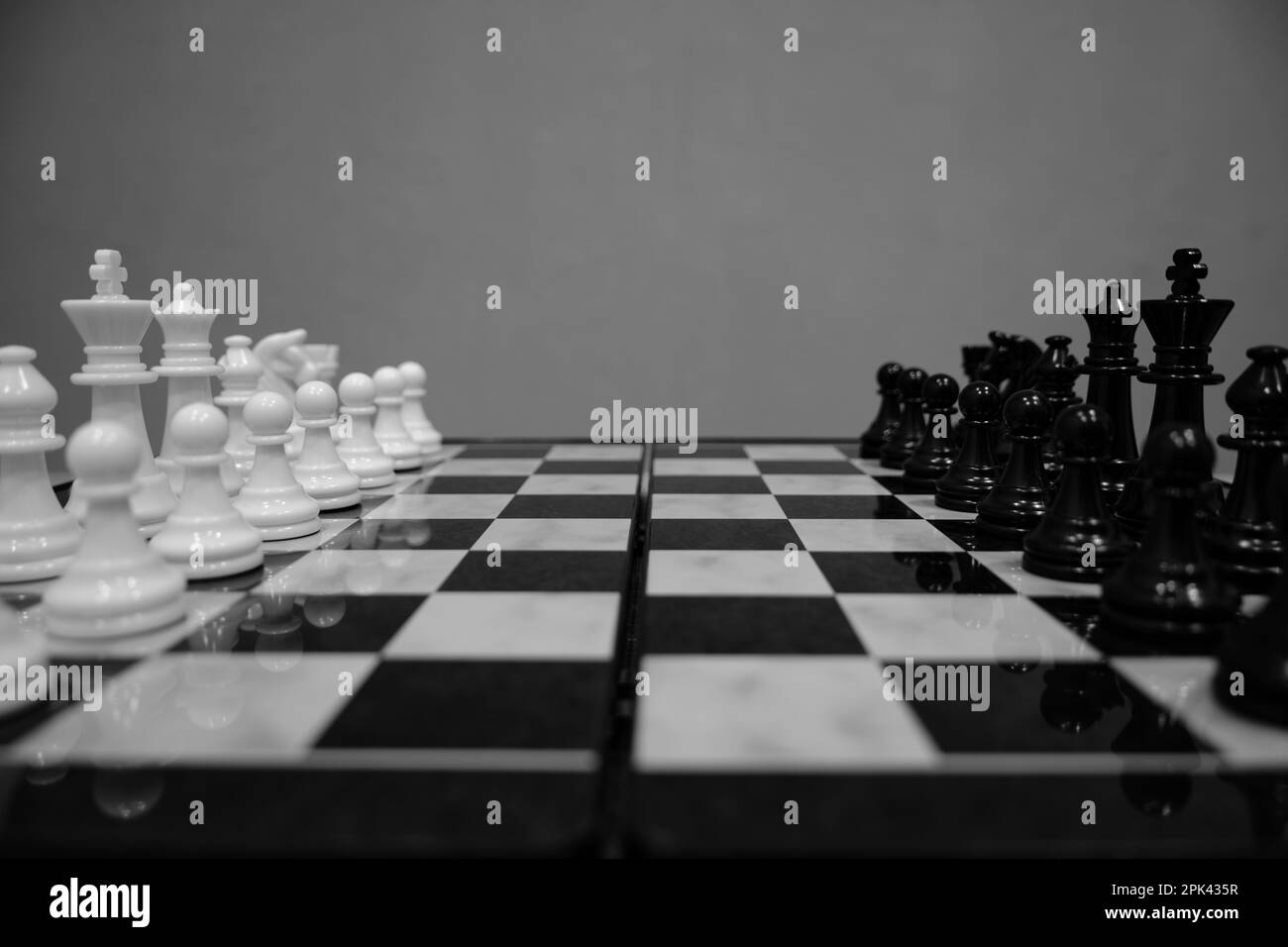 Black and white chess pieces facing each other on chessboard, on gray