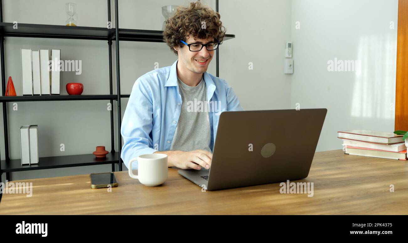 Smiling man with eyeglasses using laptop working at home Stock Photo