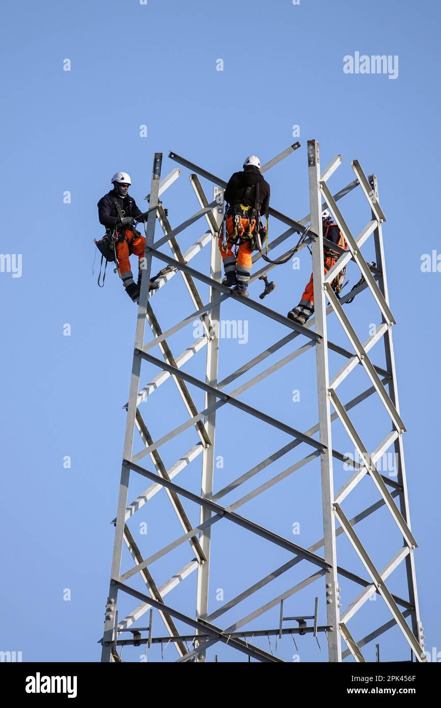 Electricians work overhead to dismantle a high voltage pylon for replacement. Milan, Italy - April 2023 Stock Photo