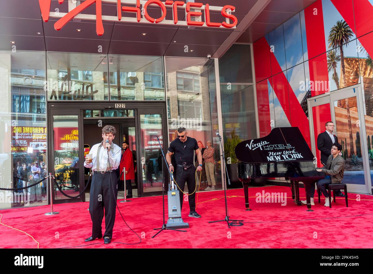Colton Ryan of the Broadway musical “New York, New York”  rehearses as a worker vacuums the red carpet at the Grand Opening of the Virgin Hotel New York in the NoMad neighborhood on Tuesday, April 4, 2023. (© Richard B. Levine) Stock Photo
