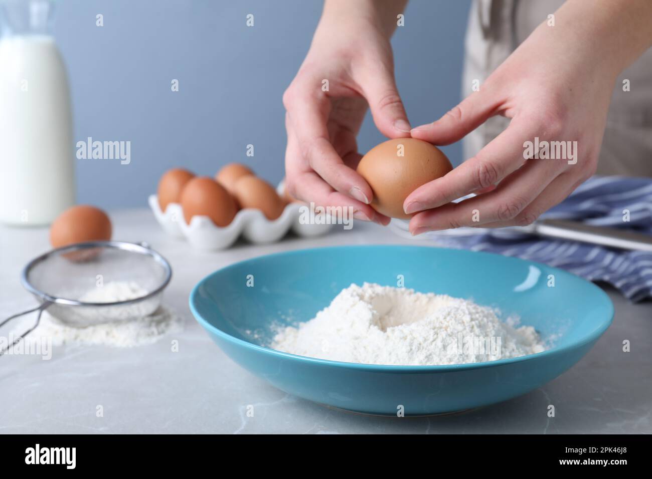 Woman preparing batter for thin pancakes at light grey table, closeup