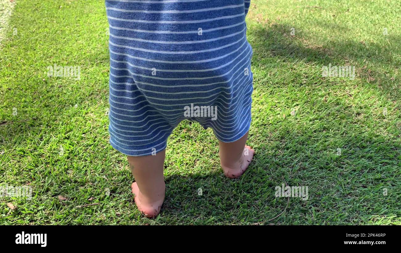 Baby toddler walking barefoot on grass outdoors. Infant child walks
