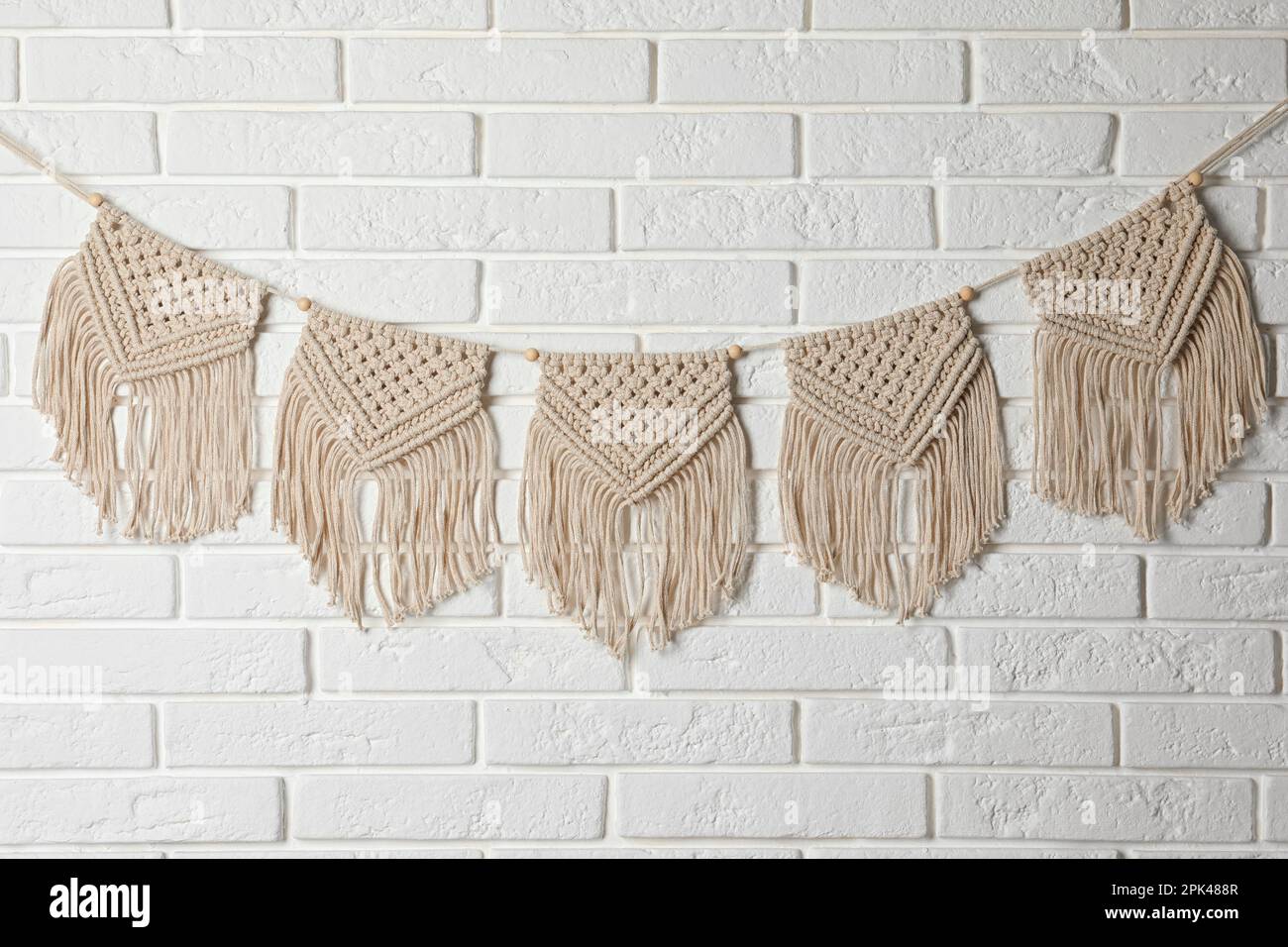 Stylish macrame hanging on white brick wall Stock Photo