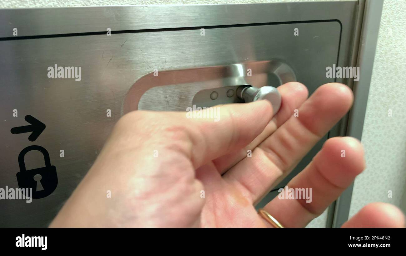 Close-up hand unlocking plane bathroom door inside airplane restroom Stock Photo