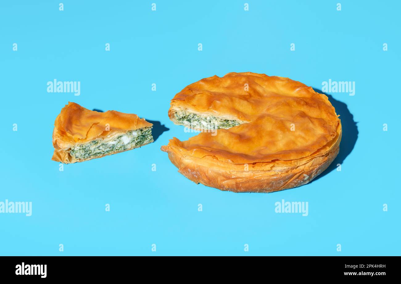 Homemade phyllo pie with cheese and spinach, minimalist on a blue table. Balkan recipe savory pie with green spinach and feta cheese. Stock Photo