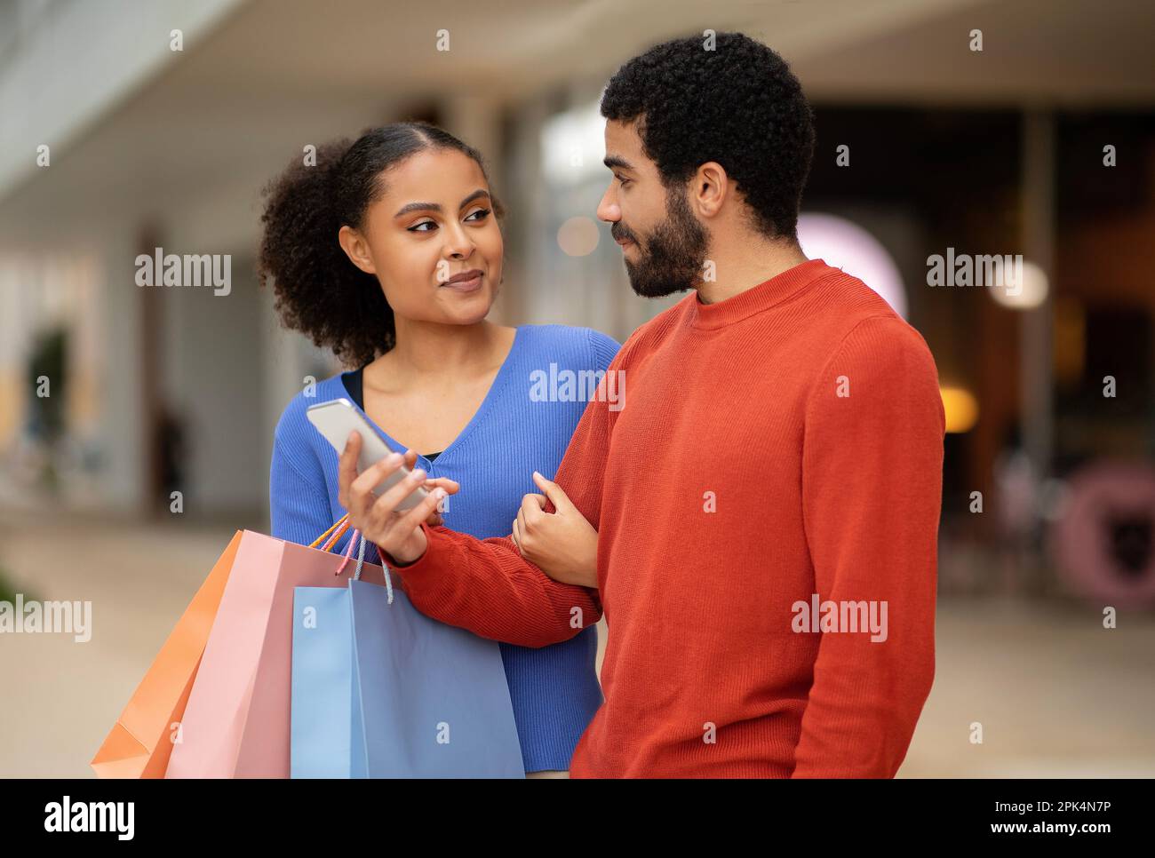 Mixed Spouses Using Mobile Shopping Application On Phone In Mall Stock Photo