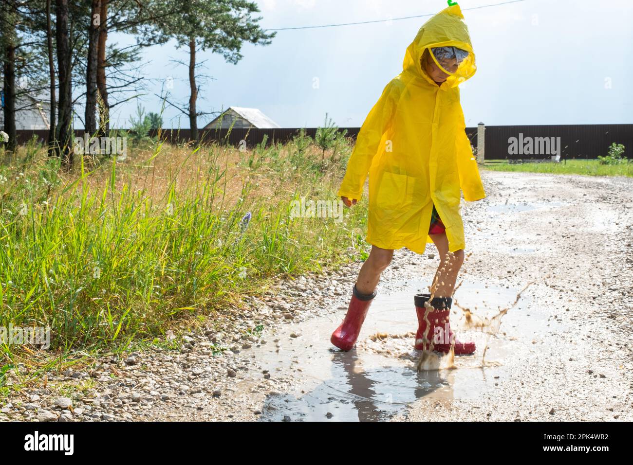 A girl in red rubber boots and a yellow raincoat runs through puddles ...