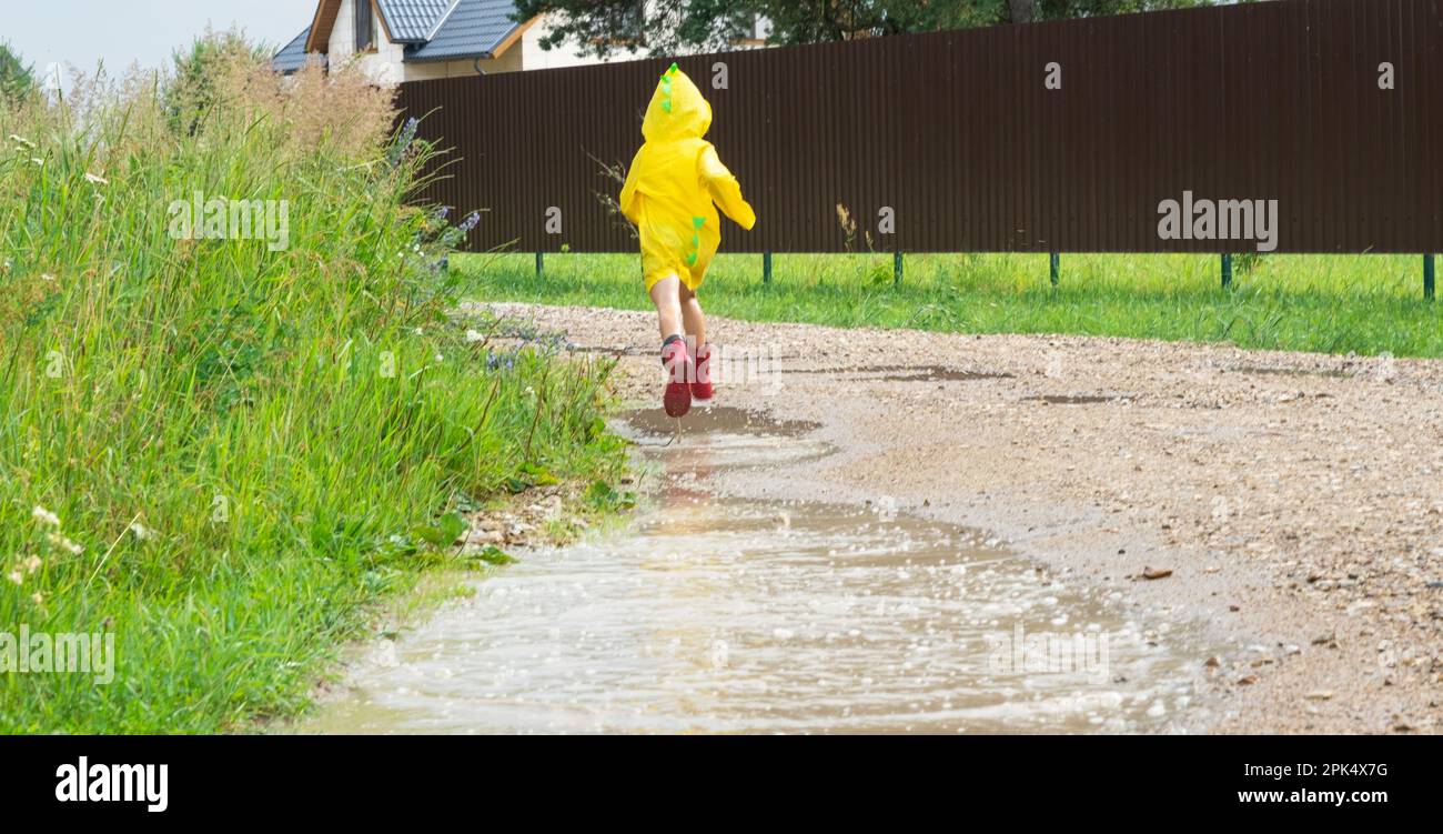 A girl in red rubber boots and a yellow raincoat runs through puddles ...