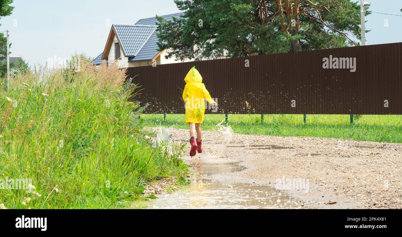 A girl in red rubber boots and a yellow raincoat runs through puddles after  a rain in the village. Summer time, freedom, childhood Stock Photo - Alamy