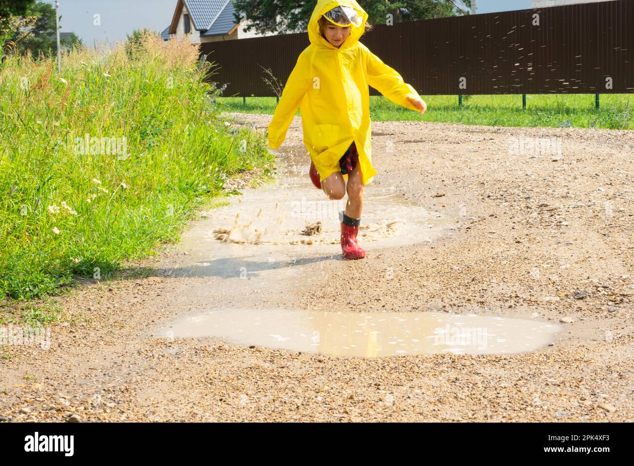 A girl in red rubber boots and a yellow raincoat runs through puddles ...