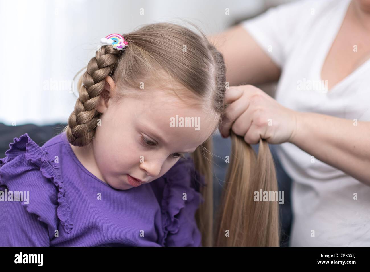 hairdresser stylist brushing child girl blond hair and styling hairdo braid hairstyle getting ready Stock Photo