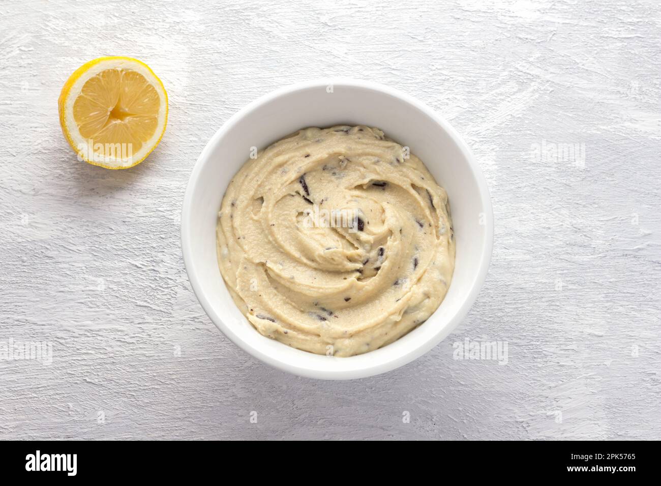 Ground in a blender soaked cashews nuts with chocolate pieces, creamy texture, with half a lemon in a white bowl on a light gray background. Cooking v Stock Photo