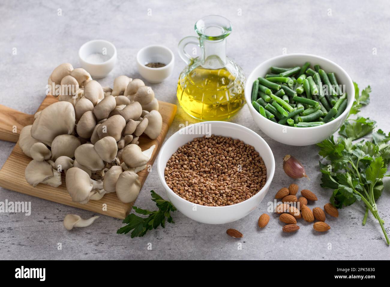 Ingredients for a vegetable vegan dish: buckwheat, oyster mushrooms, green beans, almonds, olive oil, parsley, garlic and spices on a gray background, Stock Photo