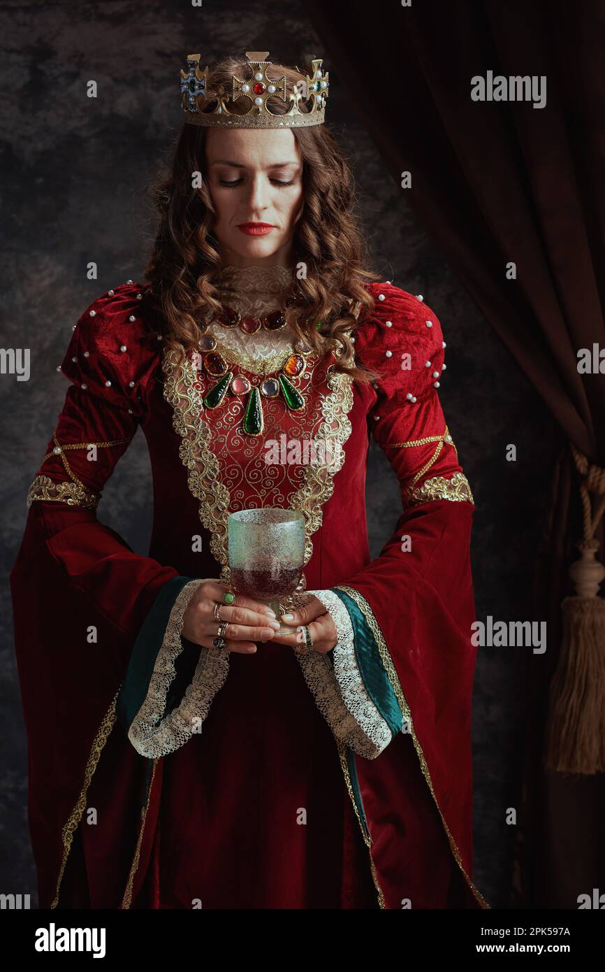 medieval queen in red dress with goblet and crown on dark gray ...