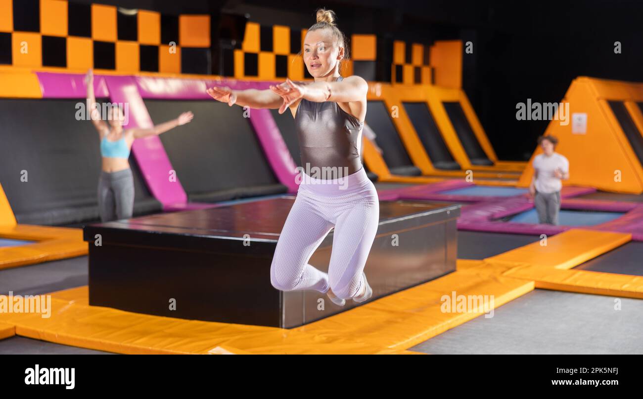 Middle-aged woman in sport clothes high jumping in trampoline arena ...