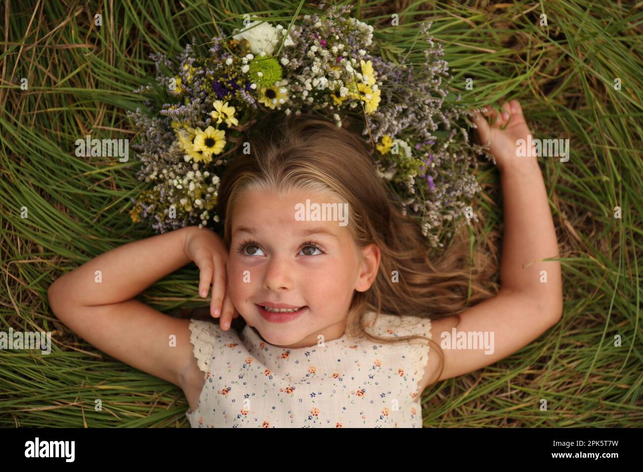 Cute little girl wearing wreath made of beautiful flowers on green ...