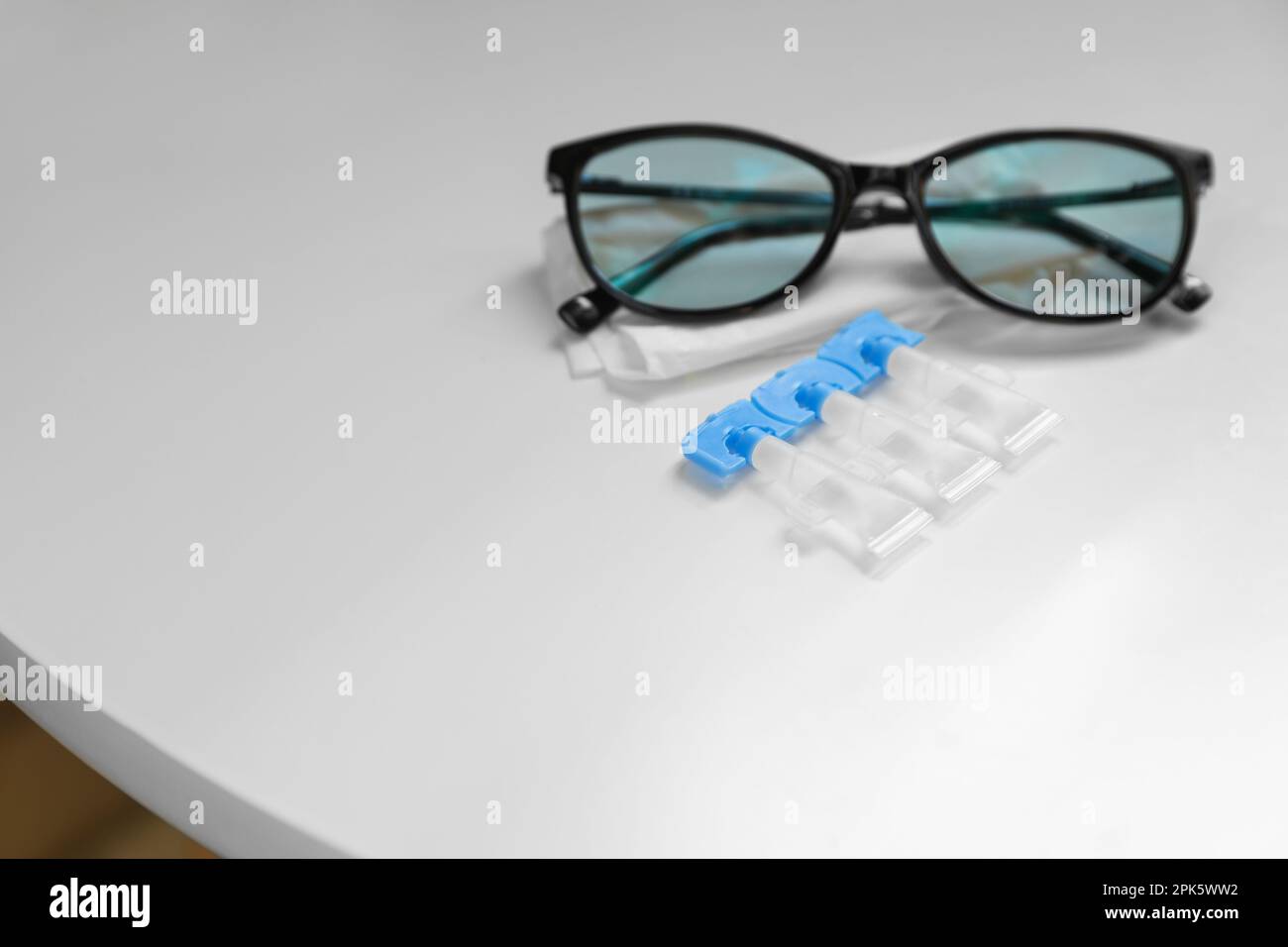 Single dose eye drops, glasses and fabric on white table, space for