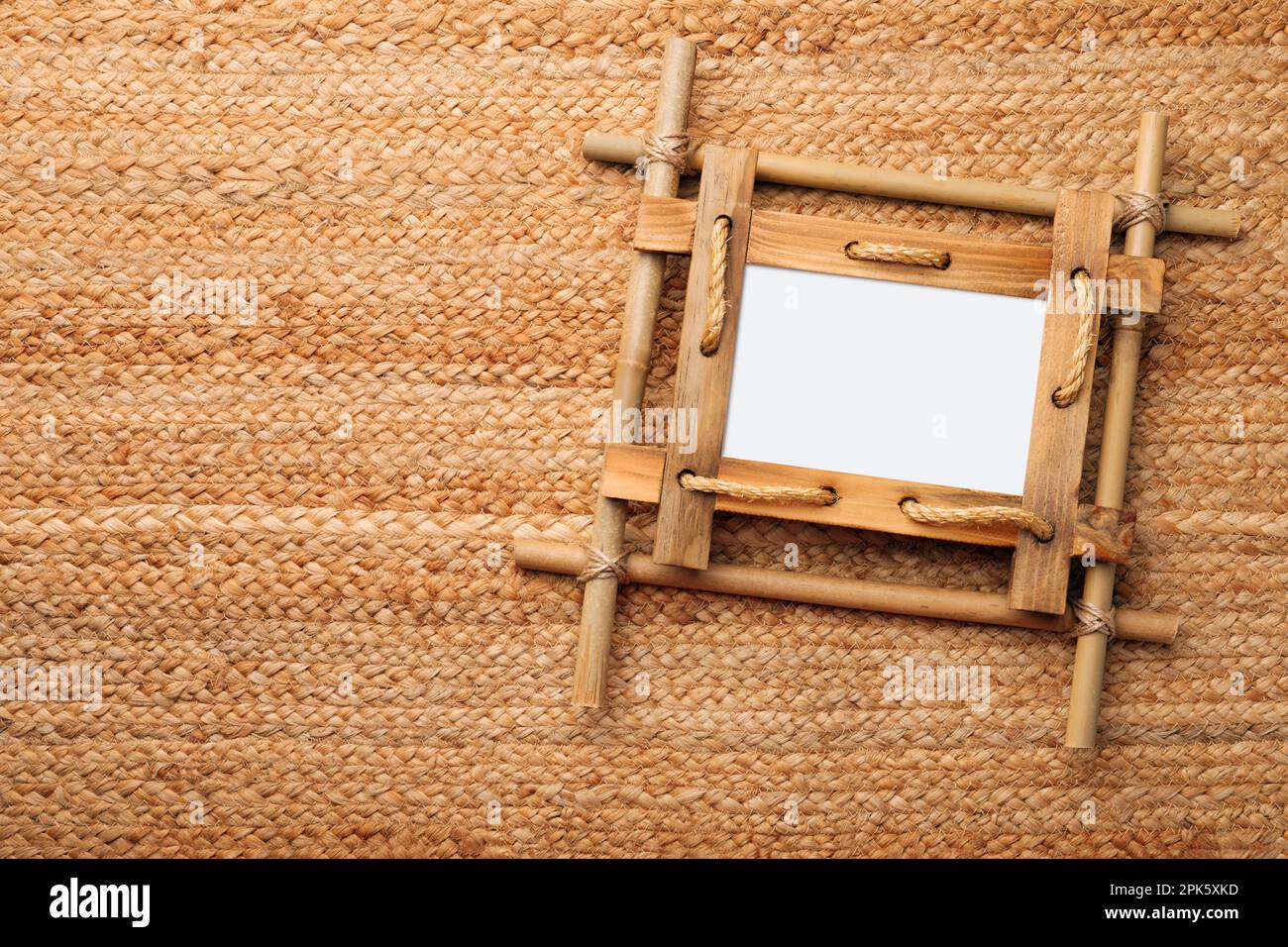 Empty bamboo frame on wicker straw background, top view. Space for text ...