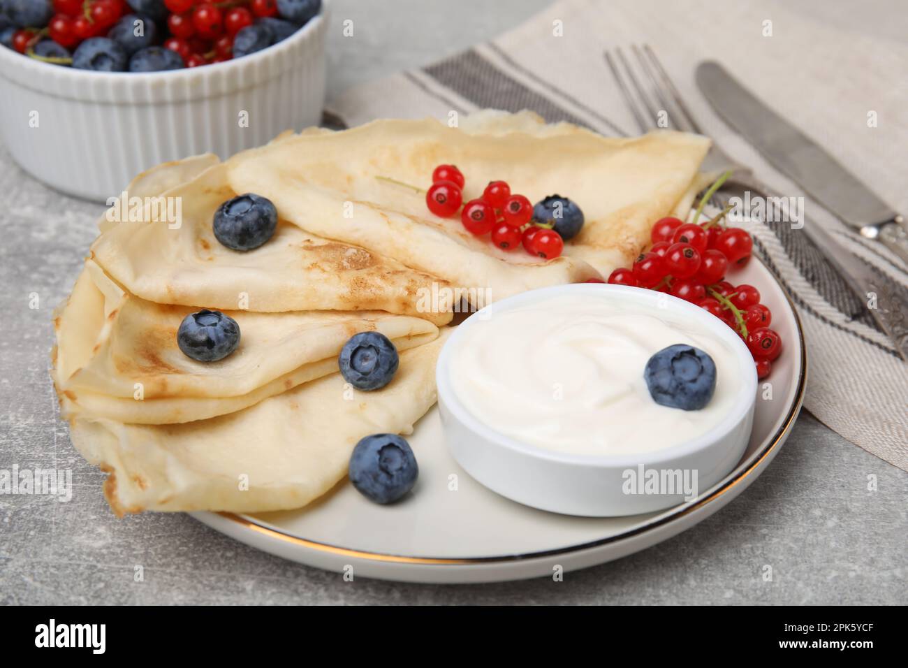 Delicious crepes with natural yogurt, blueberries and red currants on grey table Stock Photo