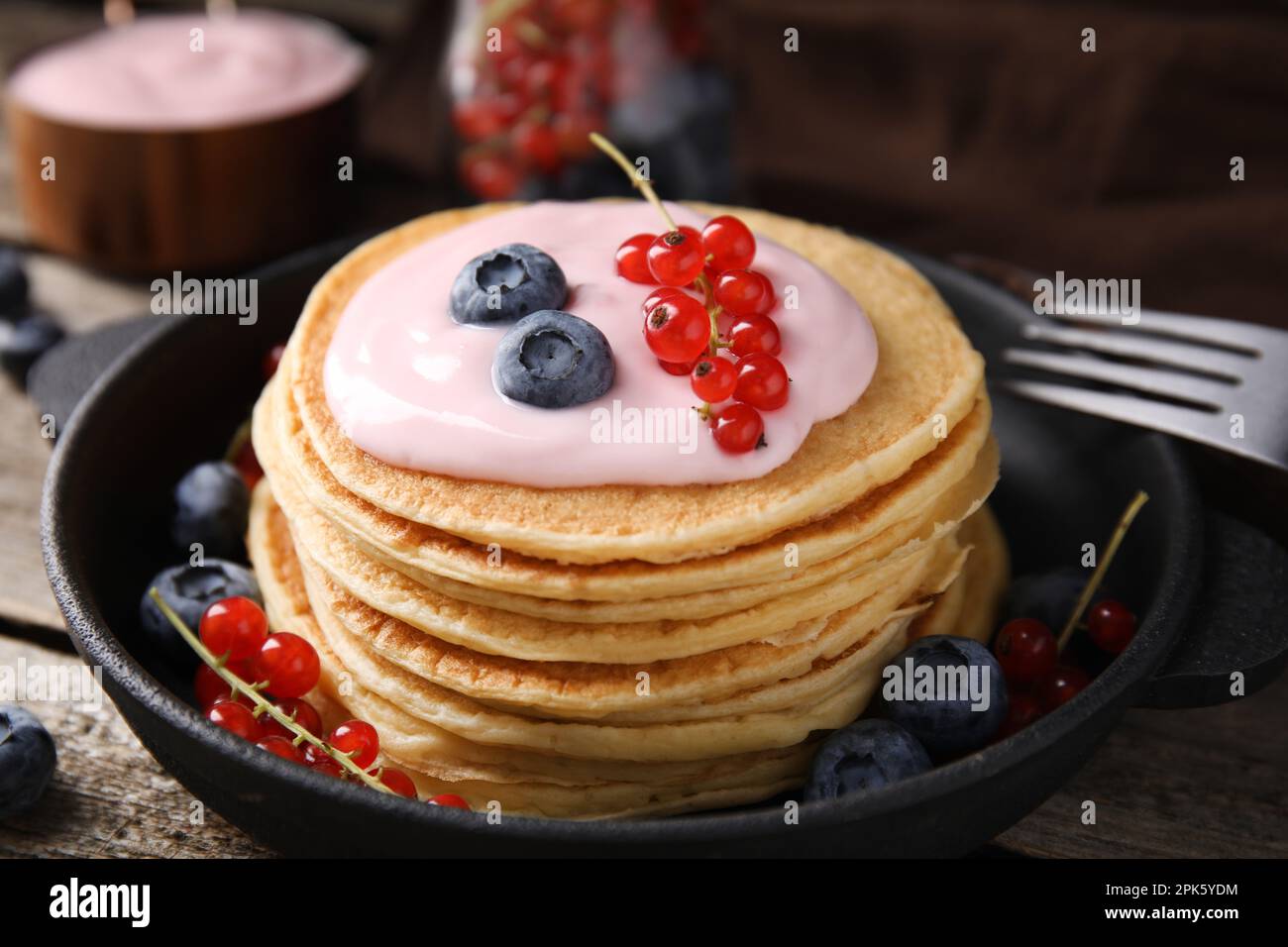 Tasty pancakes with natural yogurt, blueberries and red currants on wooden table, closeup Stock Photo