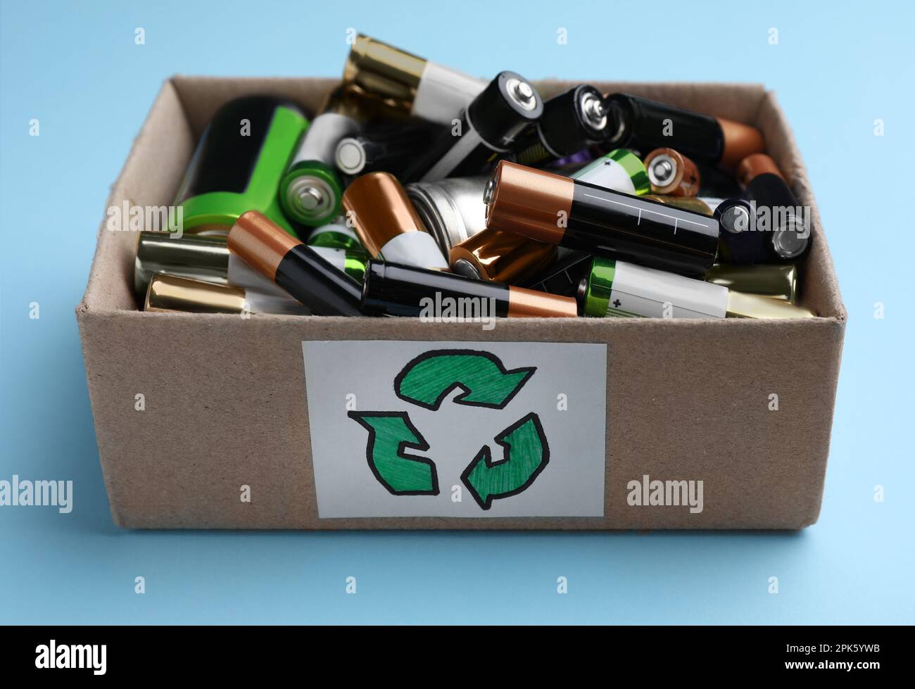 Used batteries in cardboard box with recycling symbol on light blue