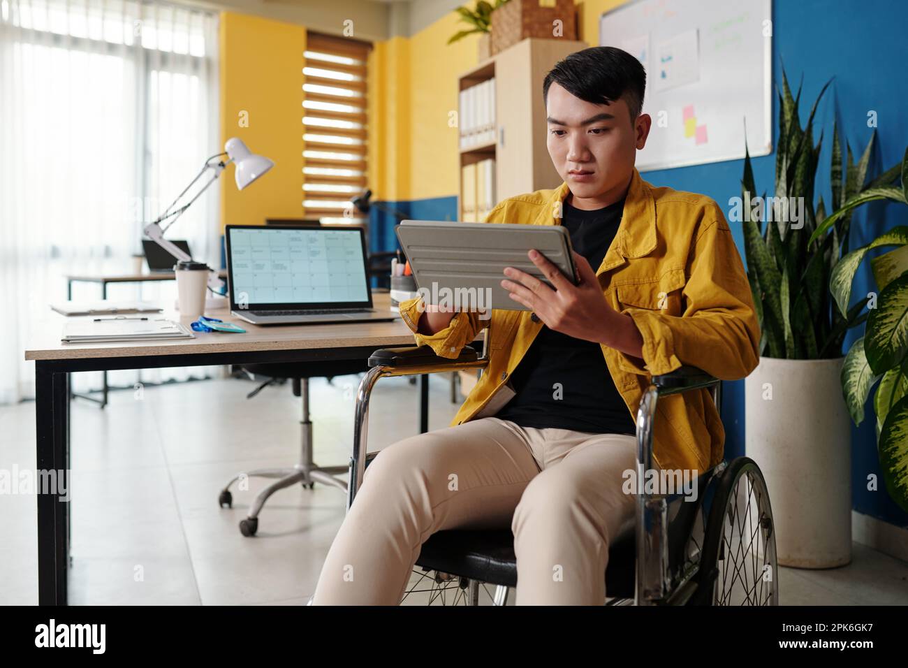 Young man with disability reading article on tablet computer when working in office Stock Photo