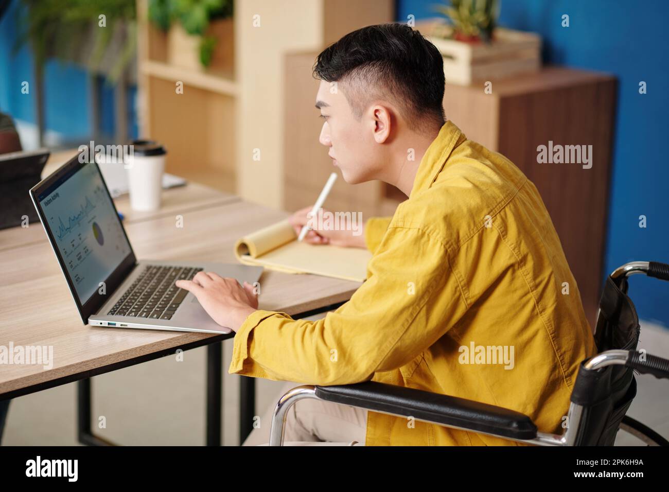 Serious businessman analyzing chart on laptop screen and taking notes in planner Stock Photo