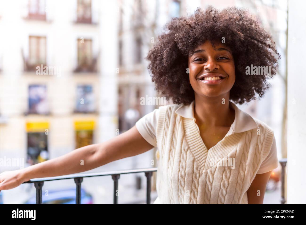 Portrait of a young black ethnic woman with afro hair on a balcony at home smiling, everyday situation, apartment Stock Photo