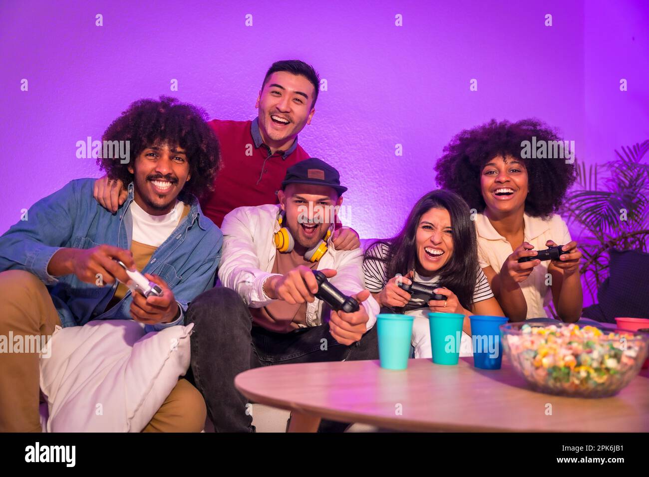 Adult party. Attractive young men sitting on the sofa playing video games with popcorn. With the joystick or controller in hand and look at the Stock Photo