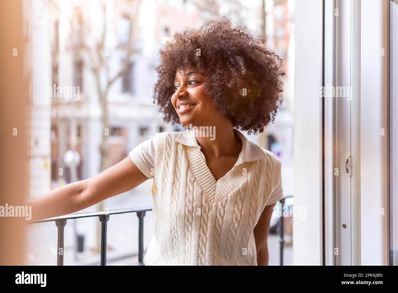Portrait of a young black ethnic woman with afro hair on a balcony at home smiling, everyday situation, at sunset Stock Photo