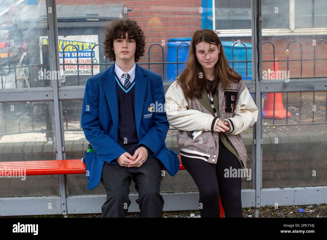 Two students waiting at a bus stop at Shankill Road in Belfast, County Antrim, Northern Ireland, UK Stock Photo
