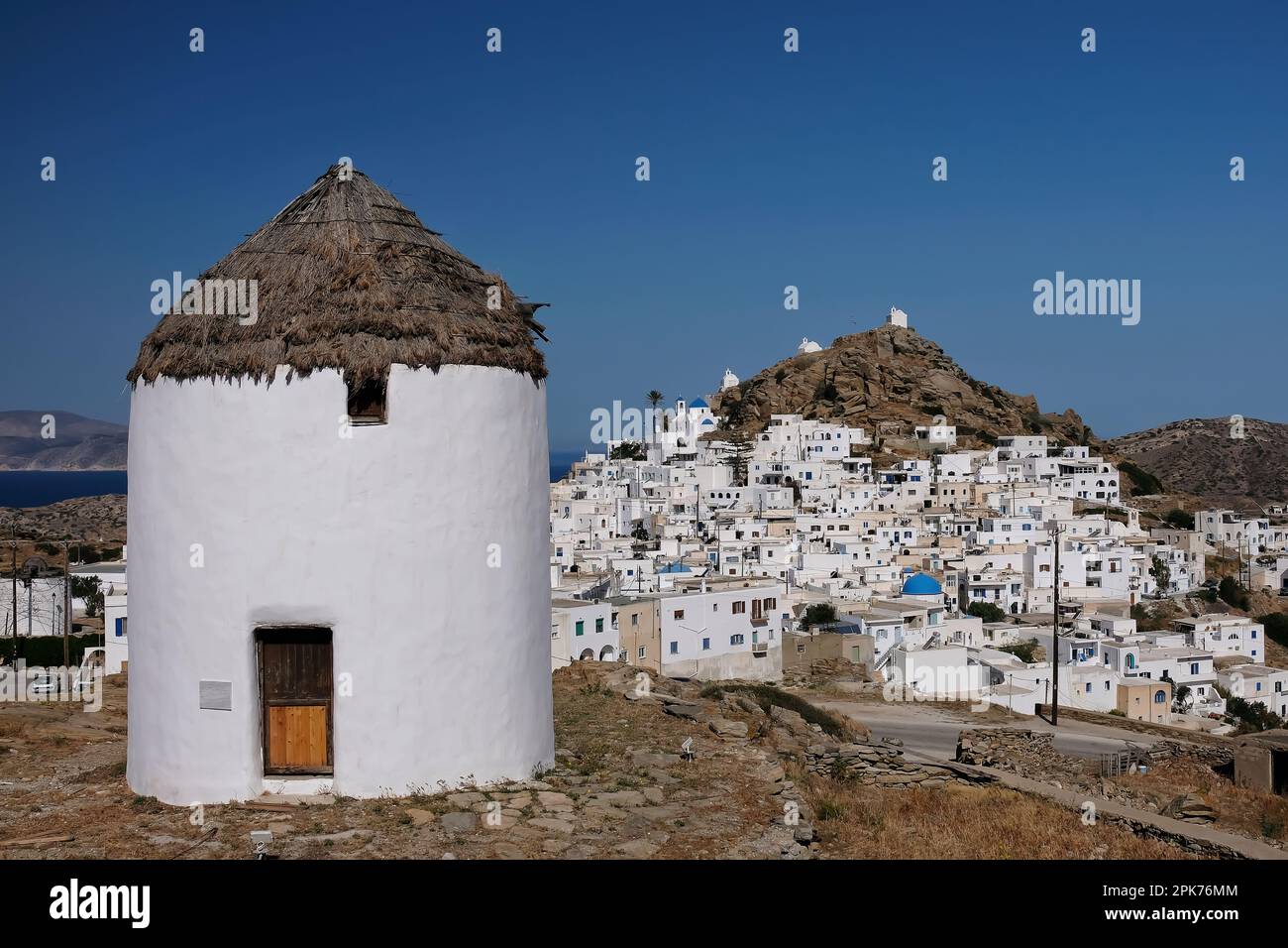 View of a beautiful white windmill and the village of Ios Greece in the backround Stock Photo