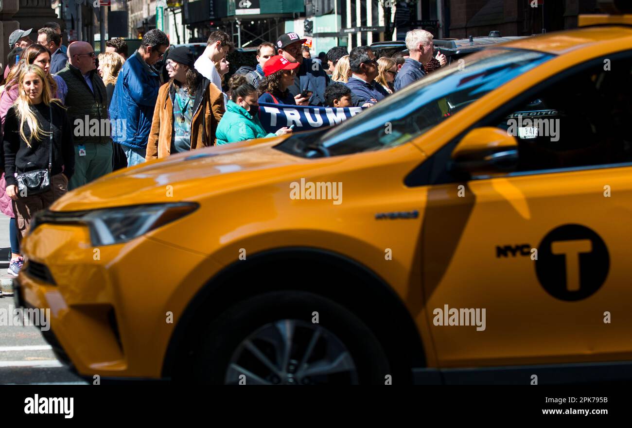 NYC Yellow Taxi drives by Trump supporters holding a Trump sign along busy 55th St and 5th Ave NYC, morning of Trump arraignment. 04 April 2023. Stock Photo
