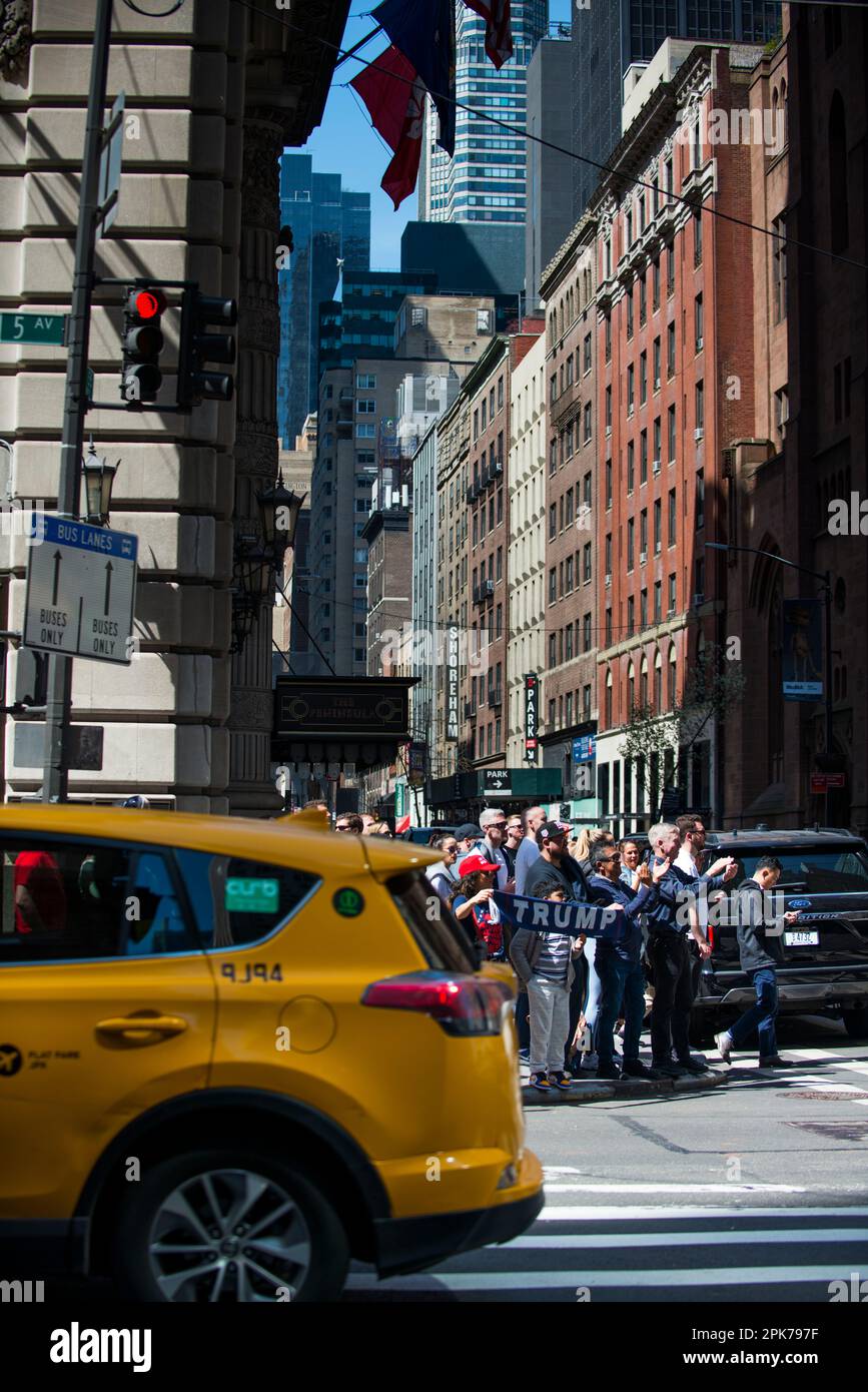 NYC Yellow Taxi drives by Trump supporters holding a Trump sign along busy 55th St and 5th Ave NYC, morning of Trump arraignment. 04 April 2023. Stock Photo