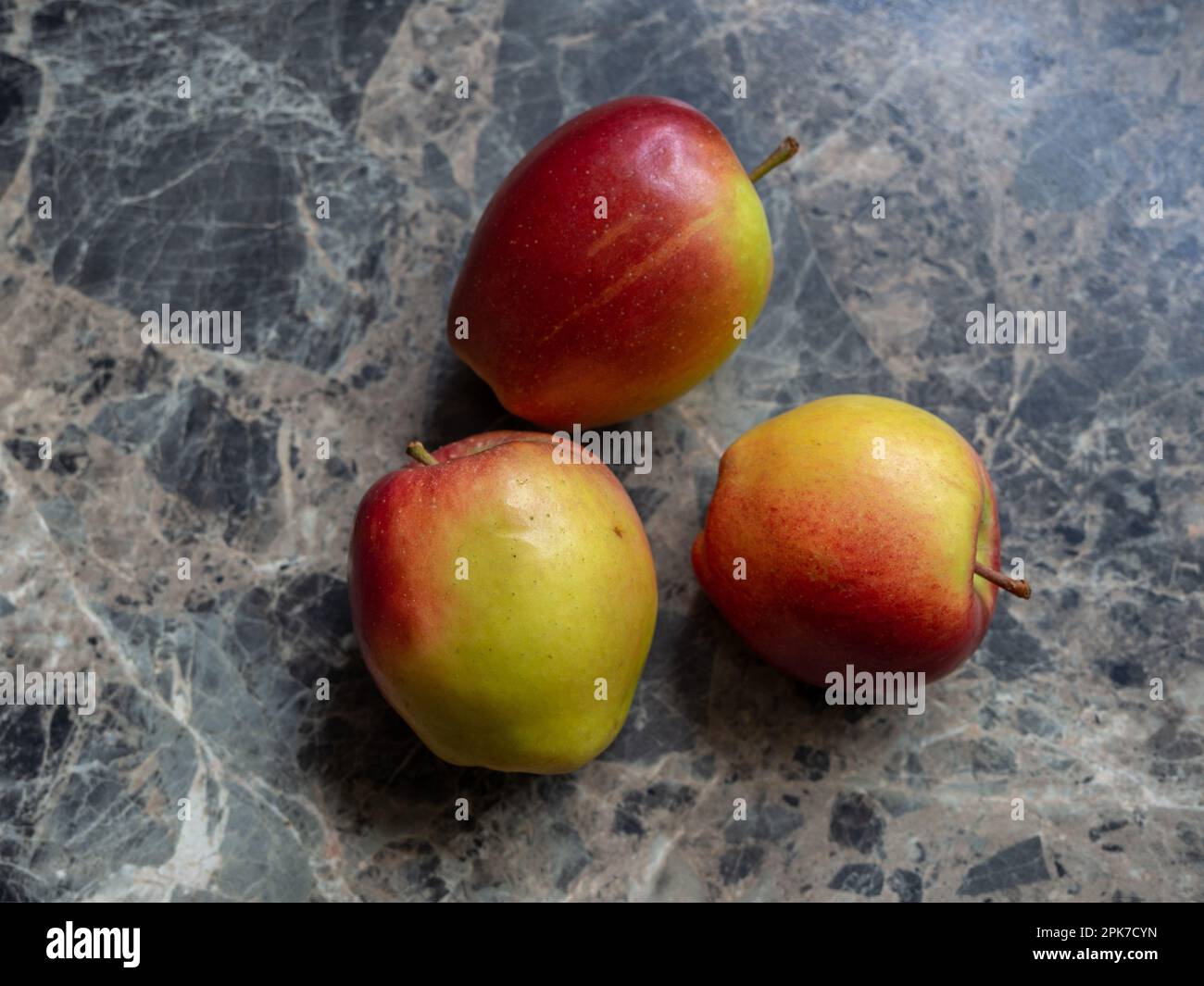 Three Braeburn apples on a black marbled kitchen worktop. Stock Photo