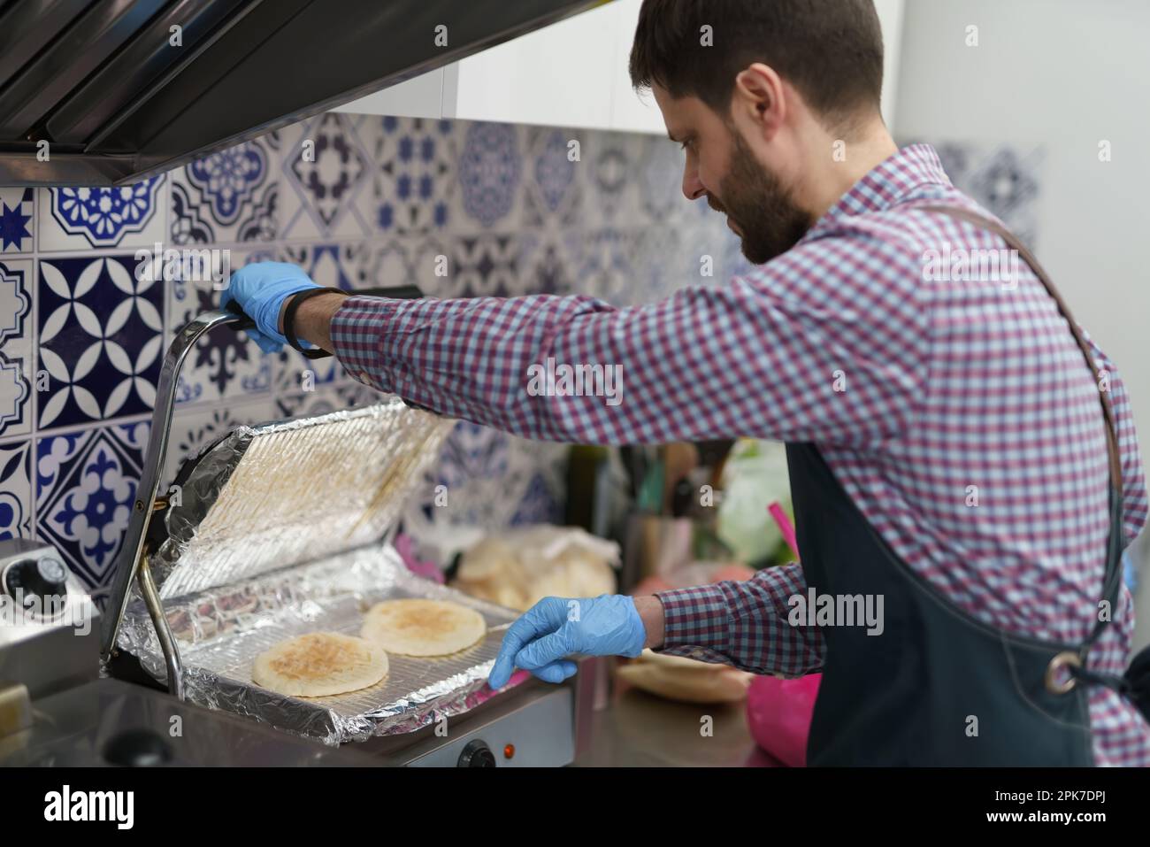 The cook toasting pita bread on a press grill in the commercial kitchen