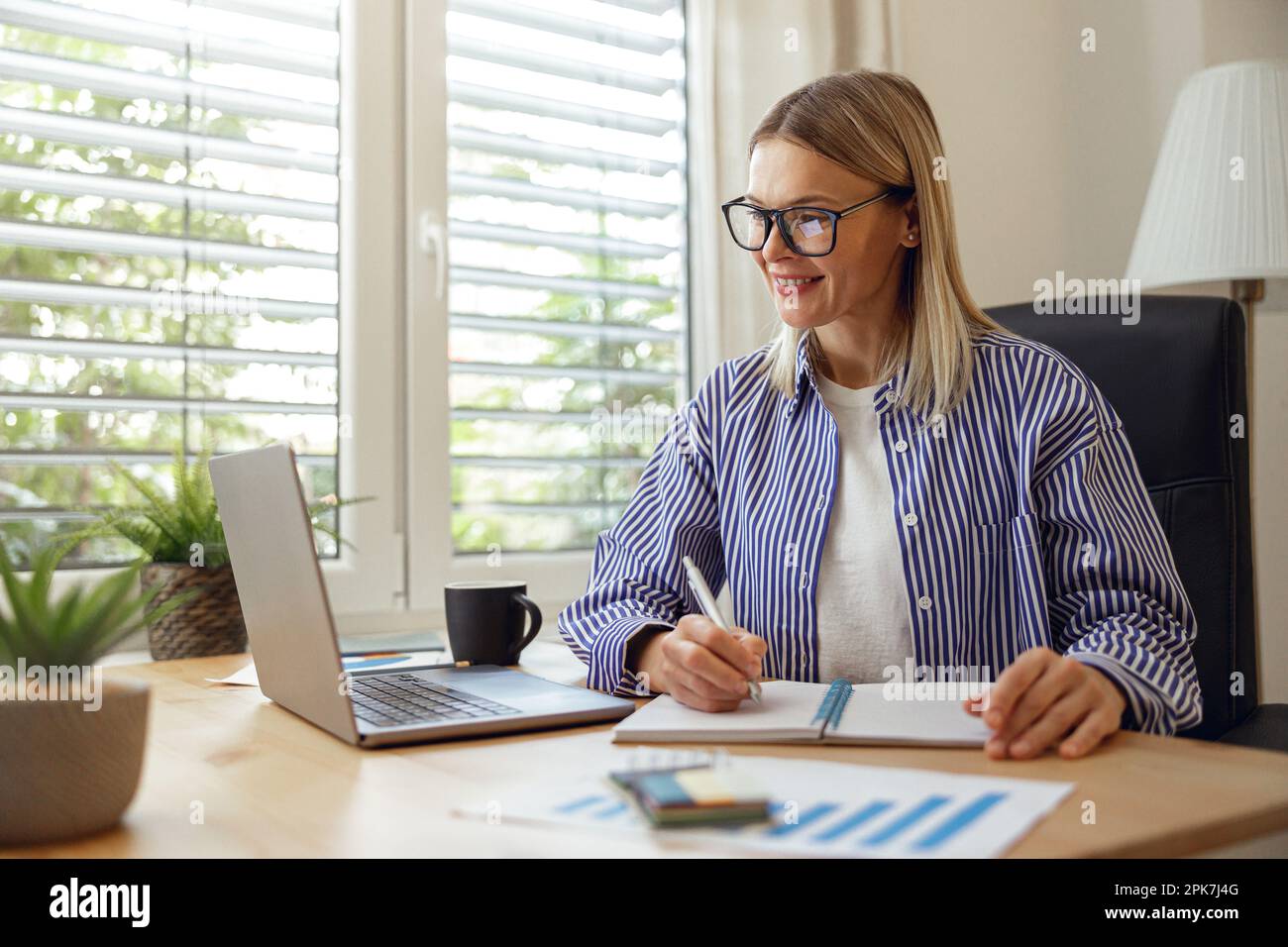 Woman freelancer making notes during online seminar while studying from home Stock Photo