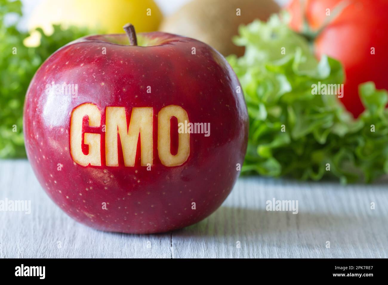 GMO text on red apple, vegetables and fruits in background, concept of genetically modified foods Stock Photo