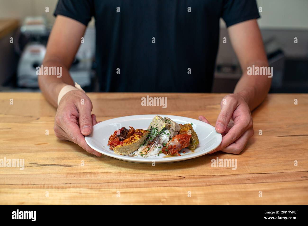 A man standing at a restaurant counter presenting plates of cooked food, menu dishes. Stock Photo